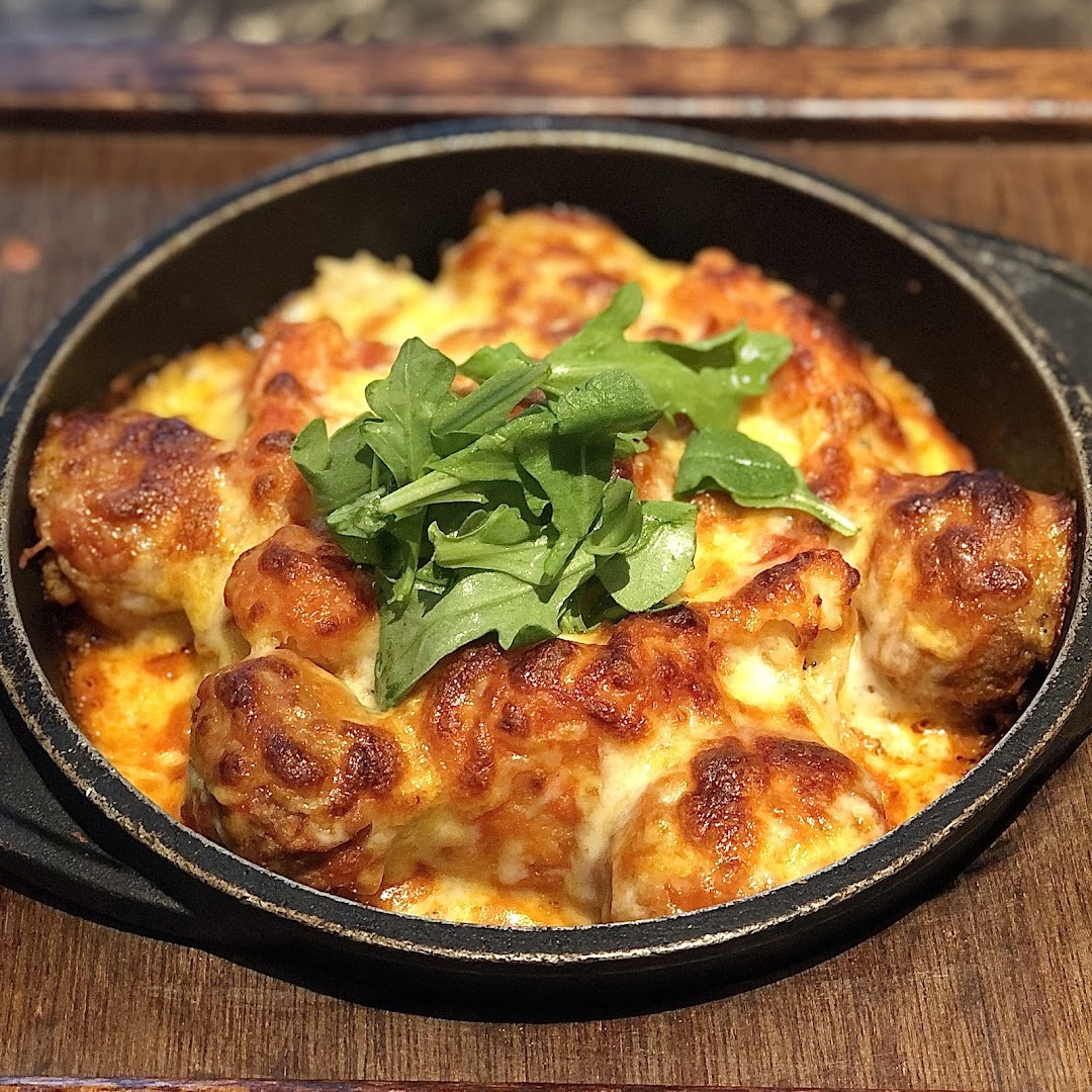A close-up of a cheesy baked dish, possibly gnocchi or pasta, topped with fresh arugula.