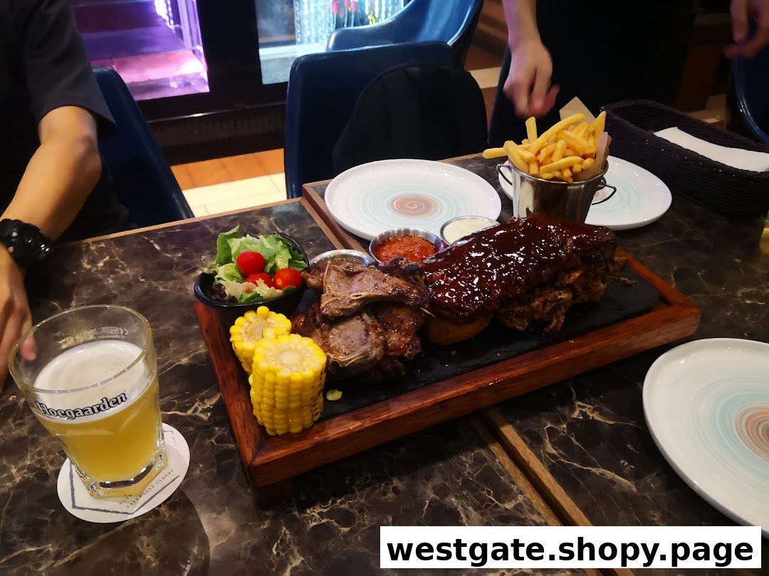A large platter of ribs, lamb chops, corn, salad, and fries with a glass of beer on a marble table.