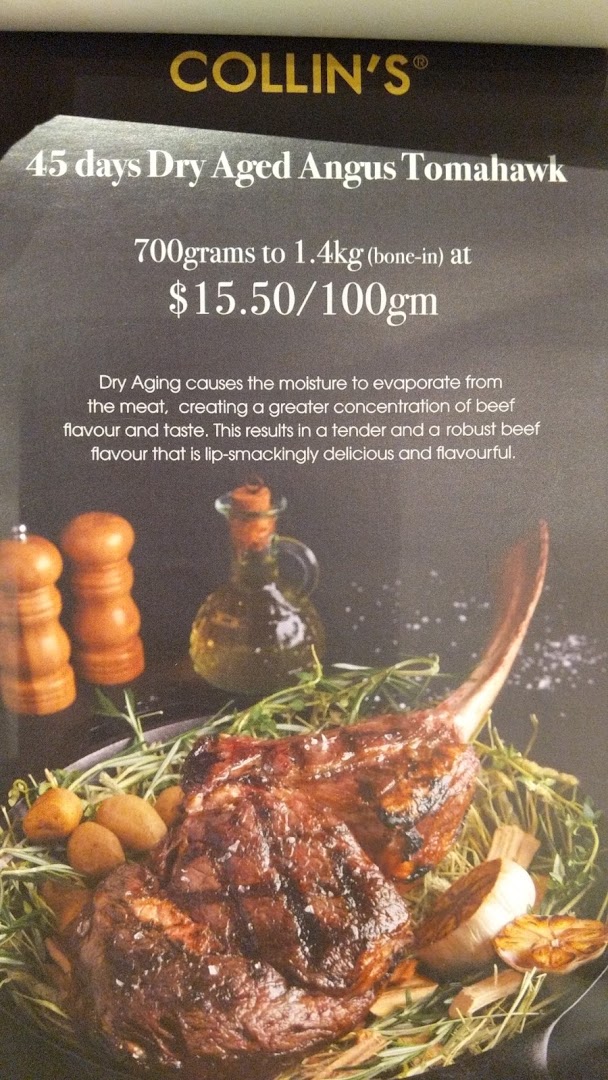 A promotional display for COLLIN'S featuring a 45-day Dry Aged Angus Tomahawk steak.