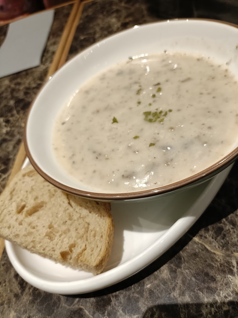 A bowl of creamy mushroom soup with a slice of bread on a marble table.