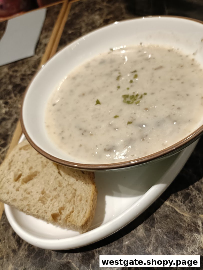 A bowl of creamy mushroom soup with a slice of bread on a marble table.