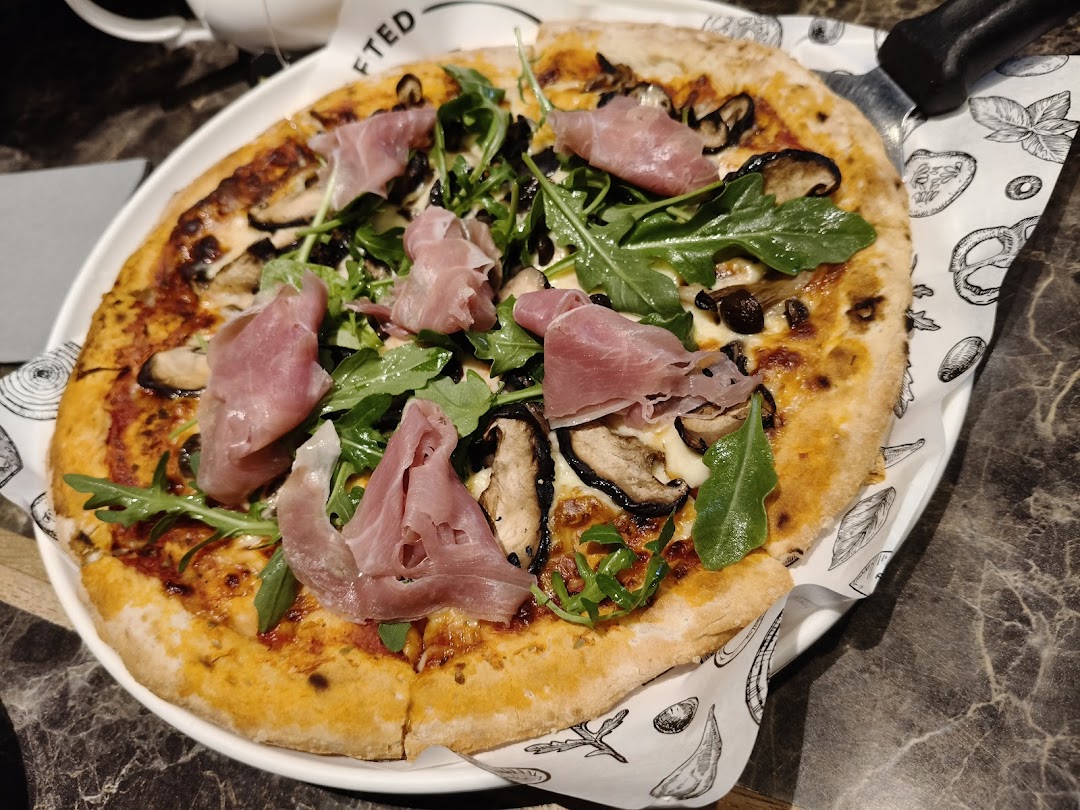 A delicious pizza topped with prosciutto, mushrooms, and arugula on a white plate.