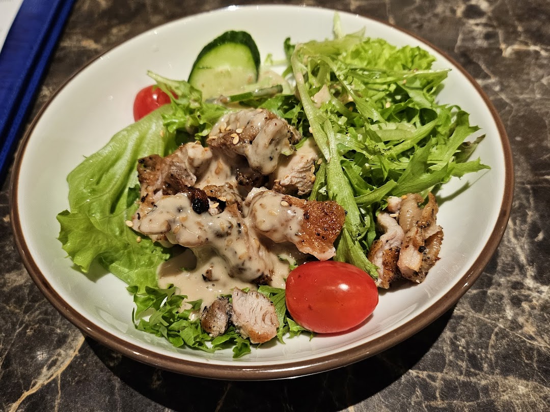 A close-up of a fresh salad with grilled meat, creamy dressing, and vegetables in a white bowl.
