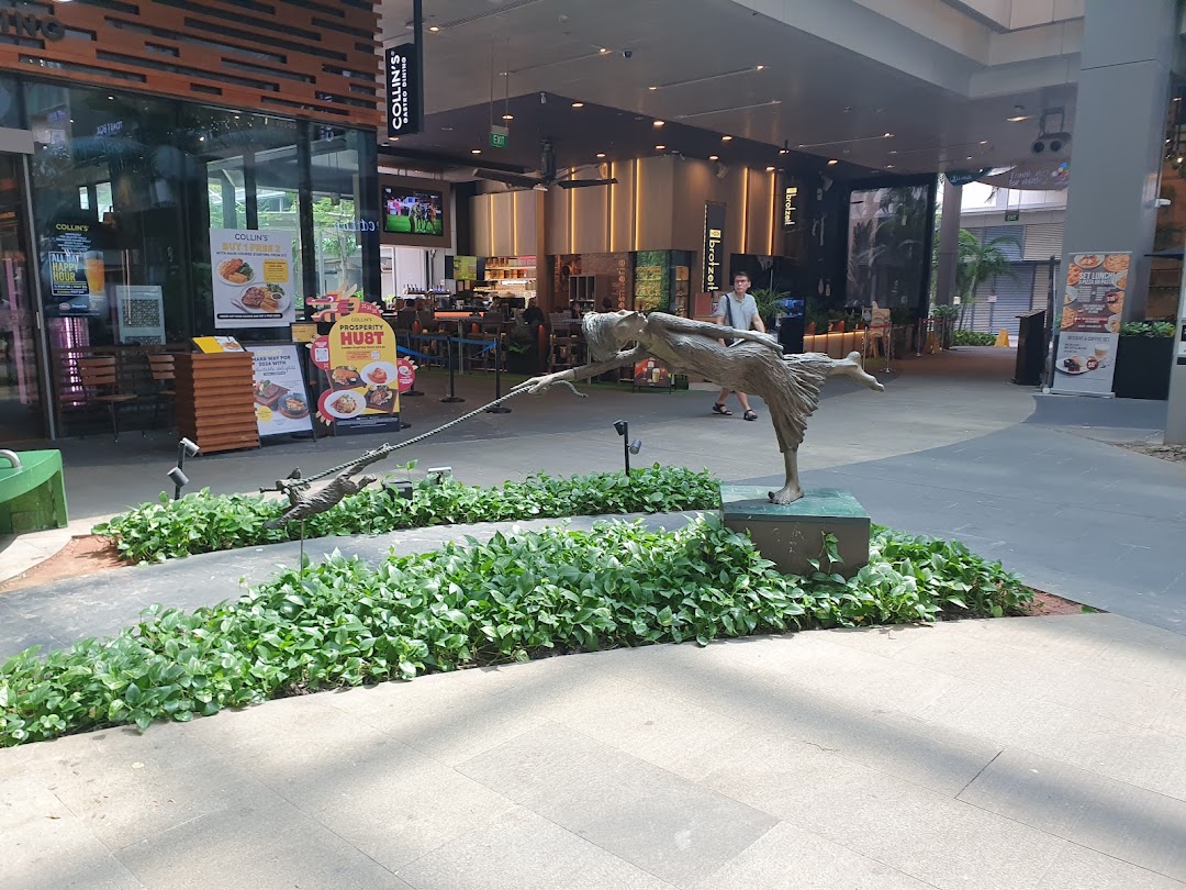 The inviting entrance of COLLINS Westgate restaurant, featuring outdoor seating, promotional displays, and a unique statue.
