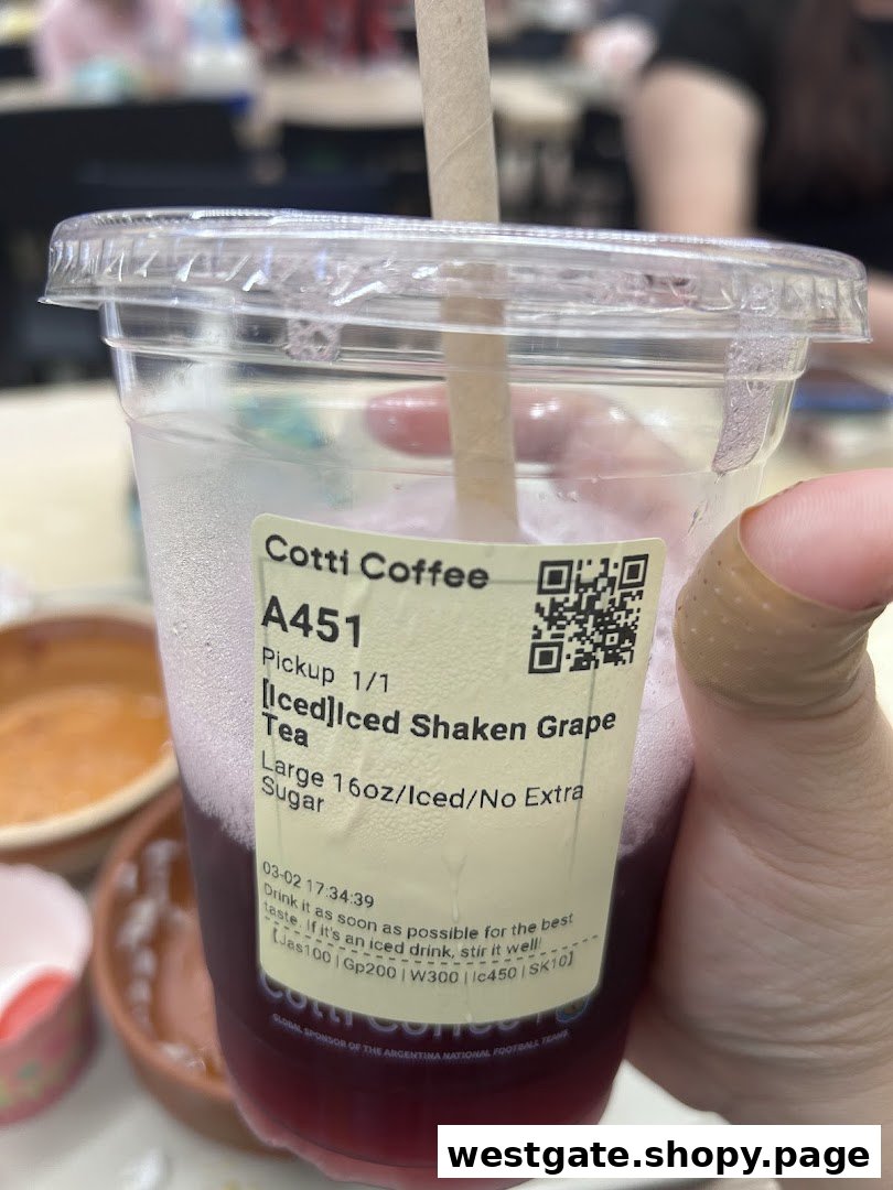 A hand holds a clear cup of Cotti Coffee's Iced Shaken Grape Tea with a label.