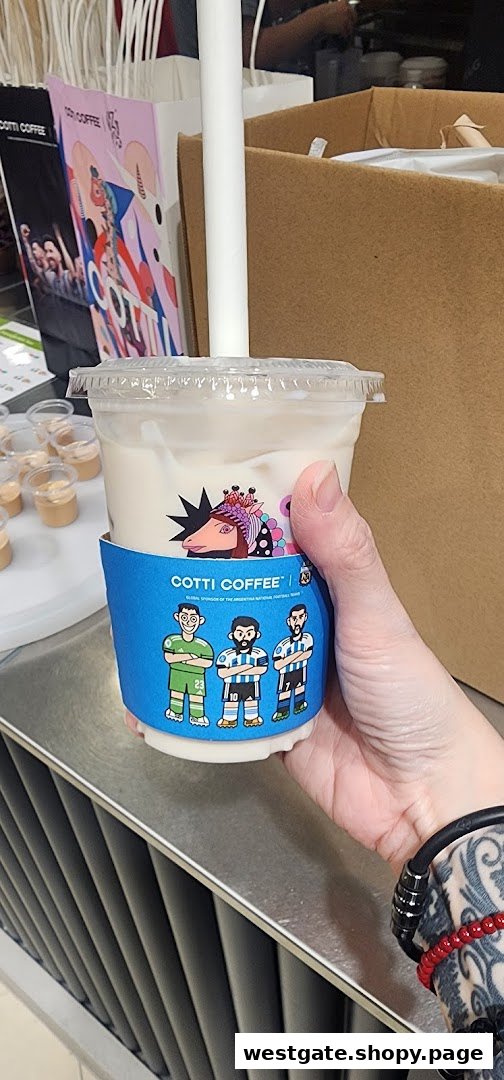 A hand holds a Cotti Coffee drink with a special blue sleeve featuring cartoon football players.