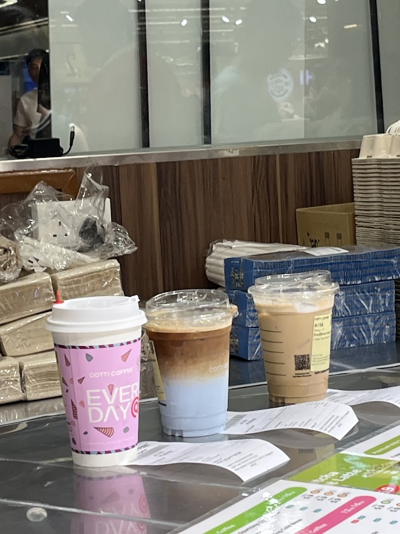 Three coffee drinks, including a unique blue-layered one, are displayed on a counter at Cotti Coffee.