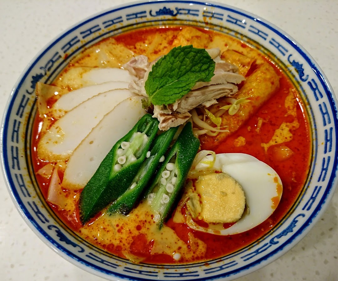 A vibrant bowl of curry noodles with fish cake, okra, chicken, and egg.