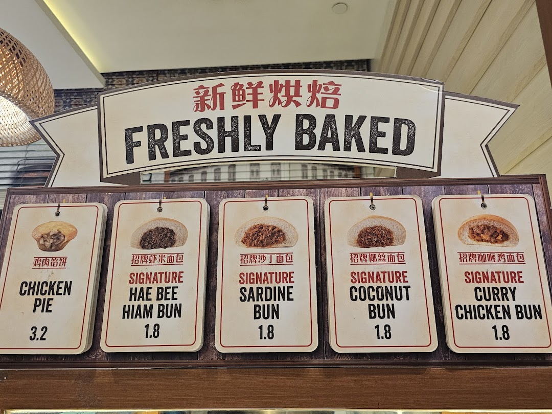 Display of freshly baked buns and a chicken pie with prices at Curry Times.