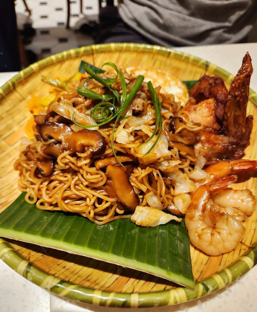 A delicious plate of noodles with mushrooms, chicken wing, and prawns served on a banana leaf.