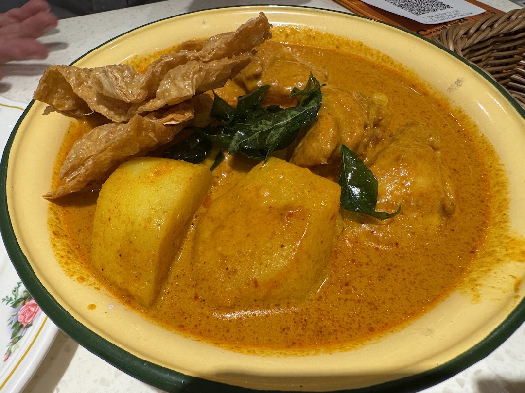 A vibrant yellow curry dish with chicken, potatoes, and bean curd skin in a traditional bowl.