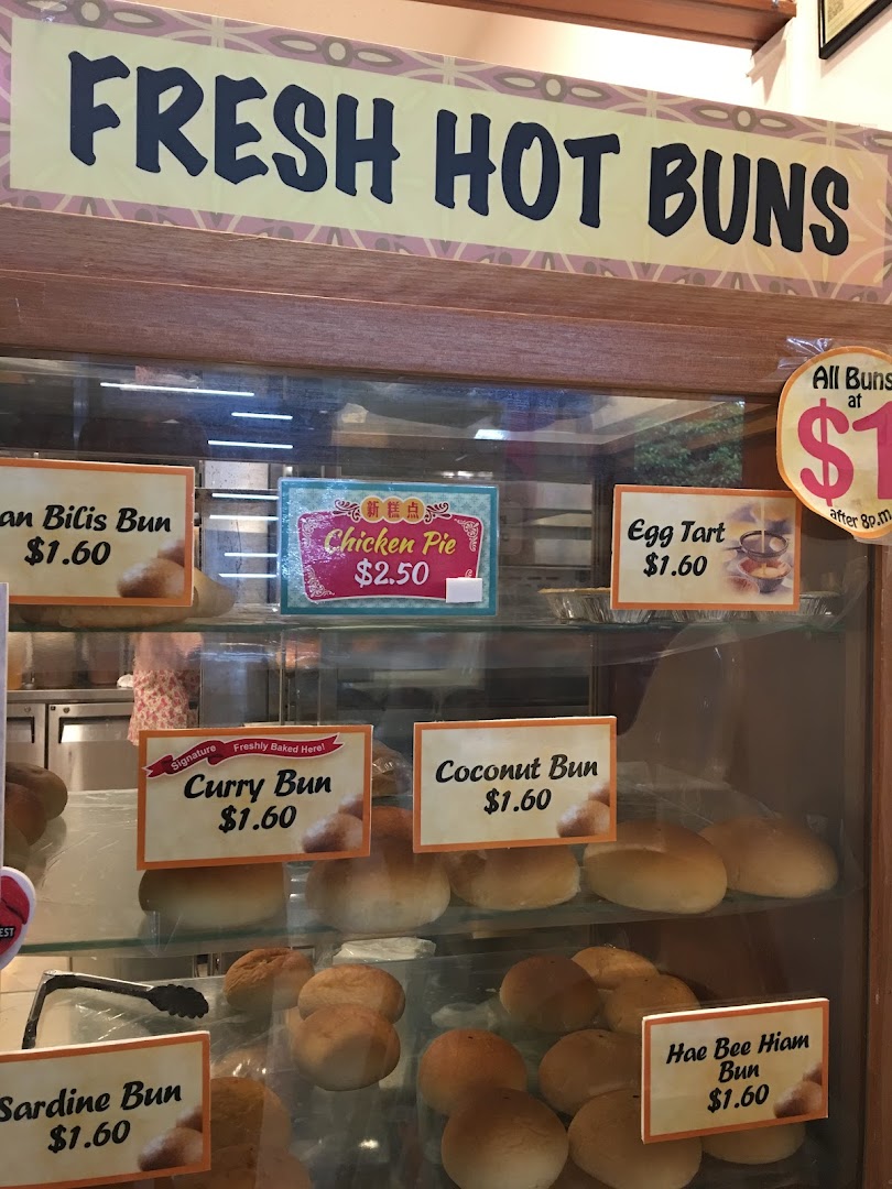 A display case showcasing a variety of freshly baked buns, pies, and tarts with prices.