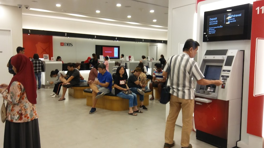Customers are seen inside a busy DBS bank branch, with some waiting and one using an ATM.