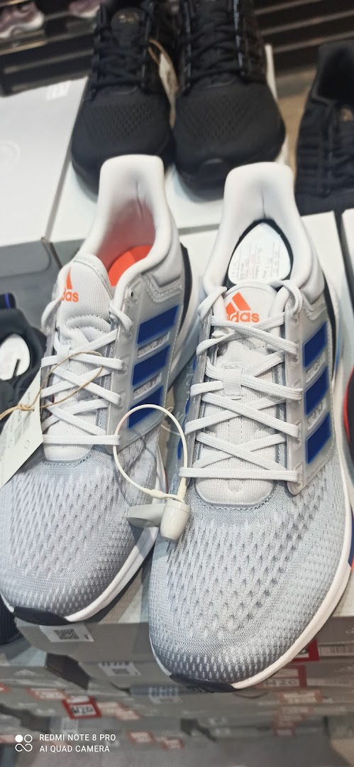 A close-up of a pair of light grey Adidas sneakers with blue stripes and orange accents, displayed in a retail store.