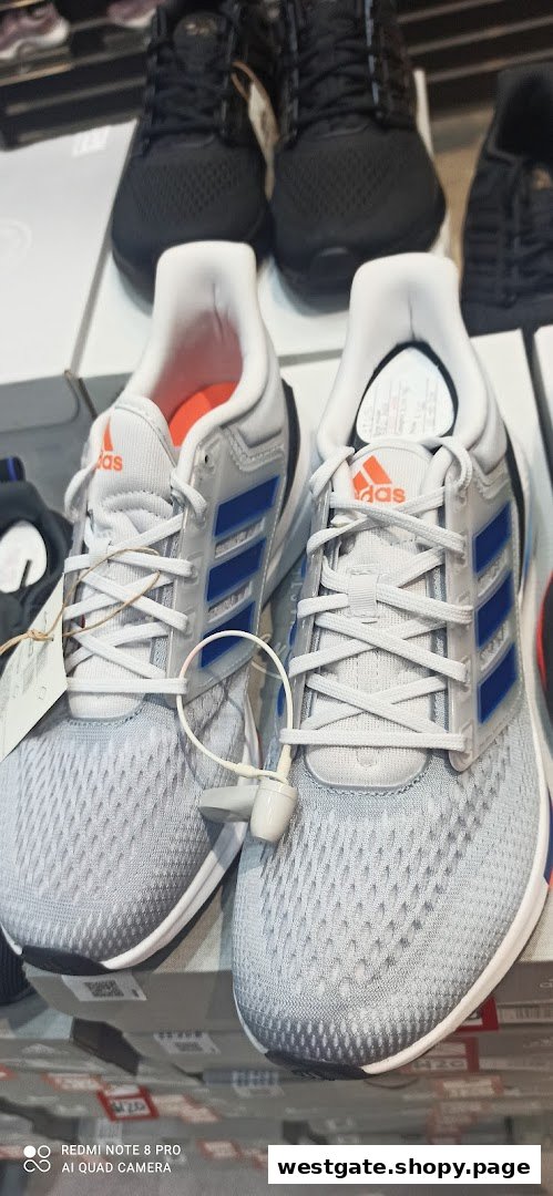 A close-up of a pair of light grey Adidas sneakers with blue stripes and orange accents, displayed in a retail store.