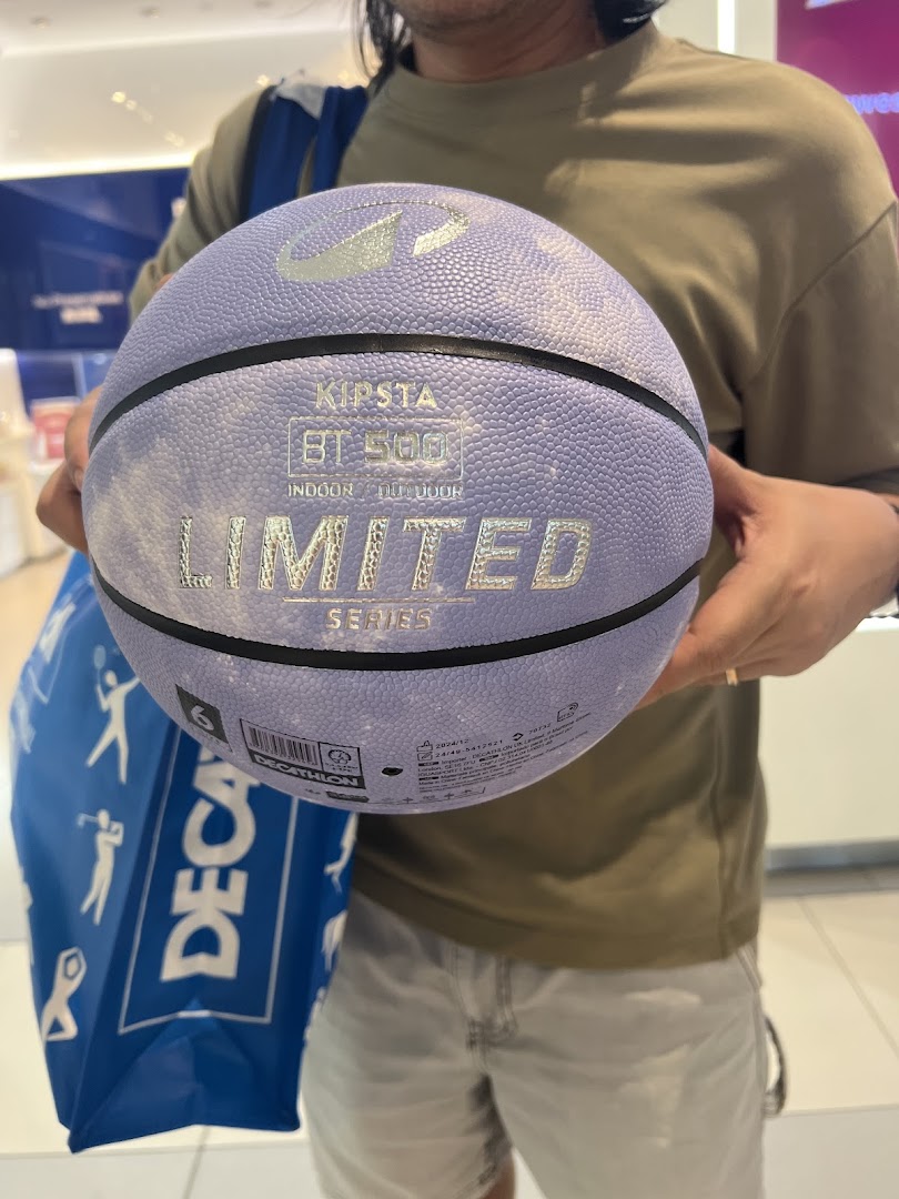 A person holds a purple Kipsta basketball inside a Decathlon store, with a Decathlon shopping bag visible.