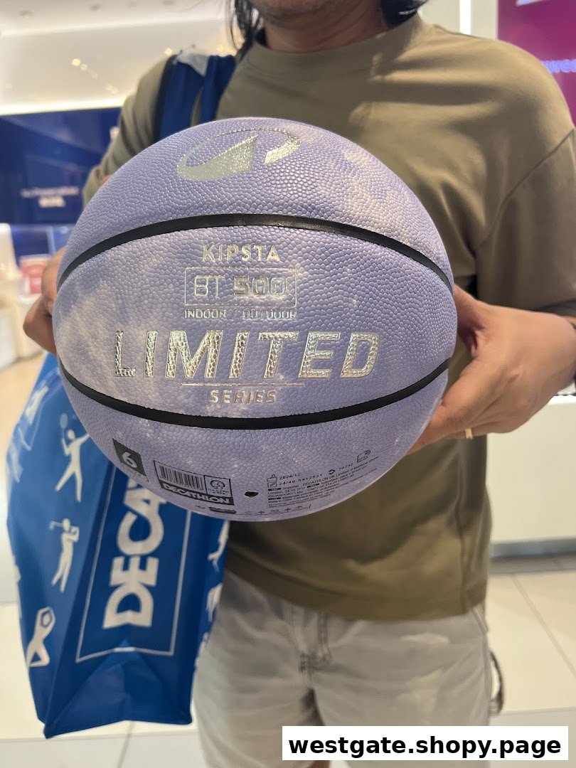 A person holds a purple Kipsta basketball inside a Decathlon store, with a Decathlon shopping bag visible.