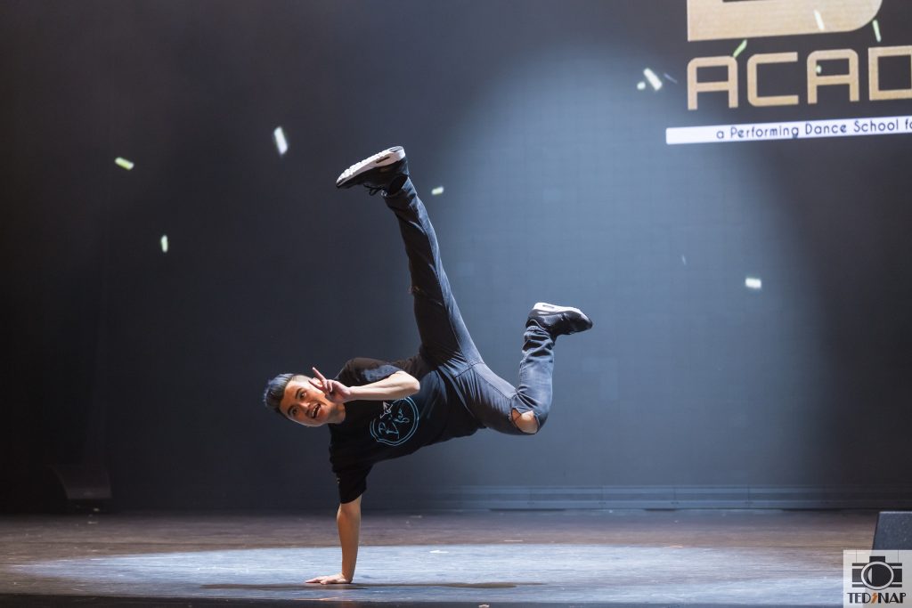 A dancer performs a dynamic breakdance move on stage at DF Academy, a performing dance school.
