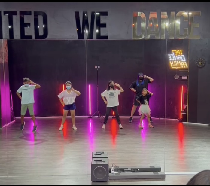 Students and an instructor practice dance moves in a modern dance studio with neon lights.