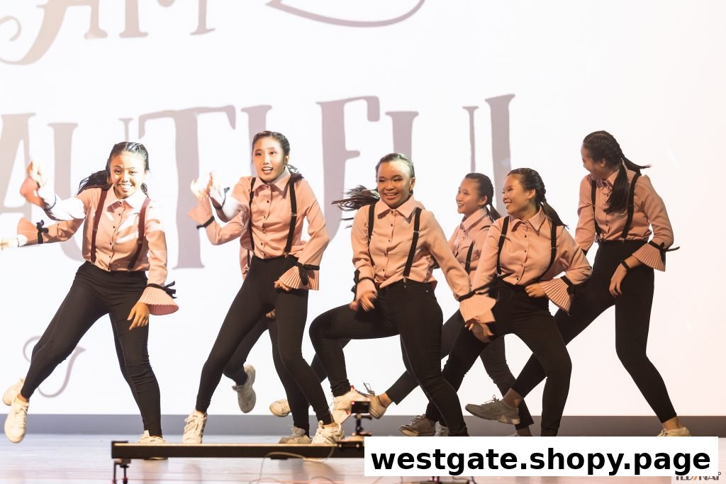 A group of young dancers in pink shirts and black pants performing on stage.