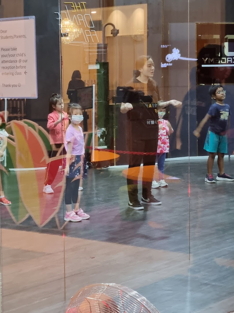 Children and an instructor engaged in a dance class, viewed through a glass window.