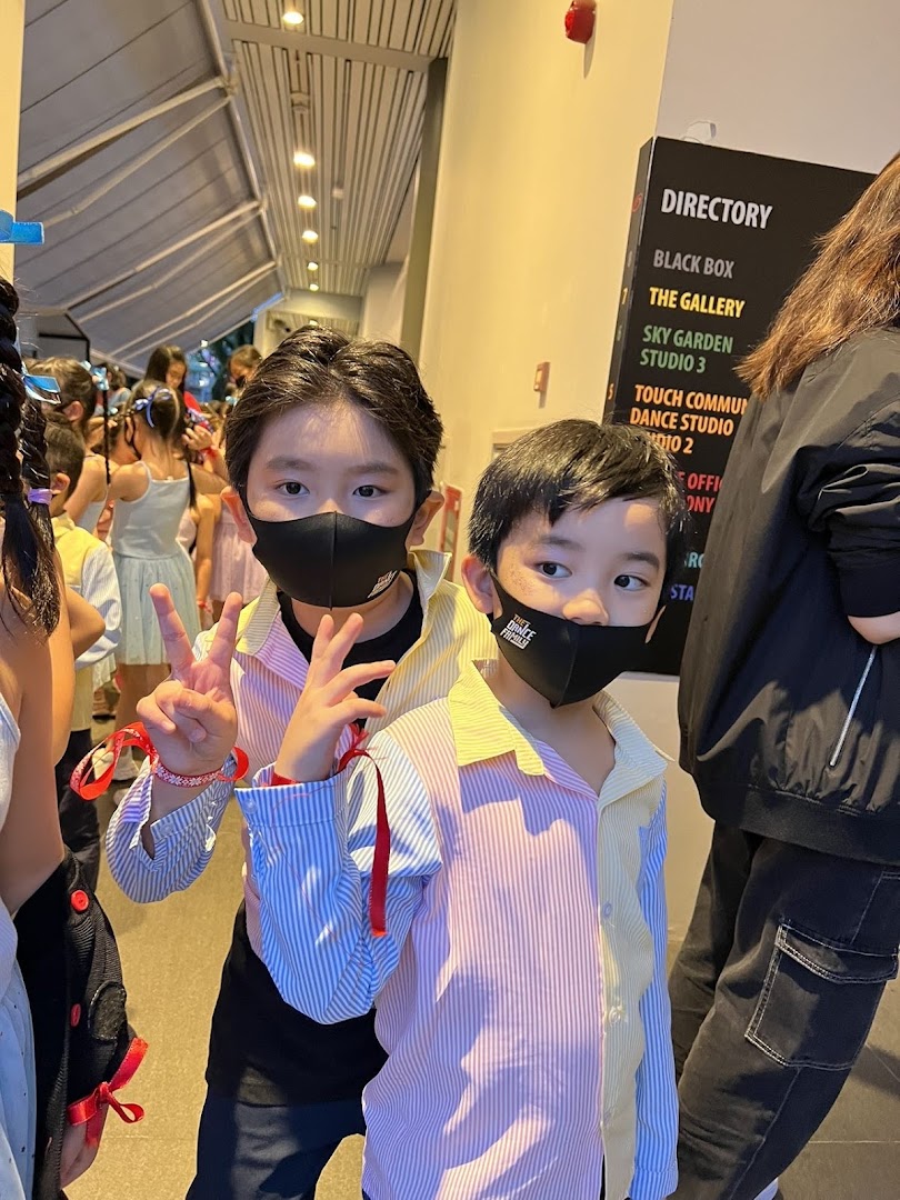 Two masked children pose in a hallway, with a directory sign and other students in the background.