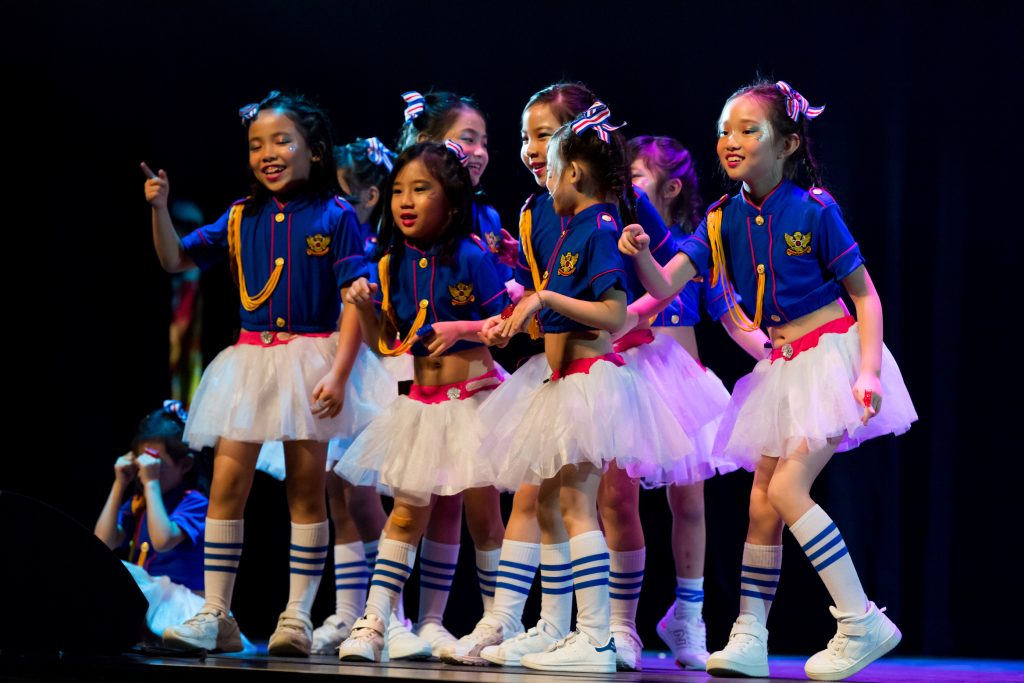 Young girls in vibrant costumes perform on stage, showcasing their talent and joy.