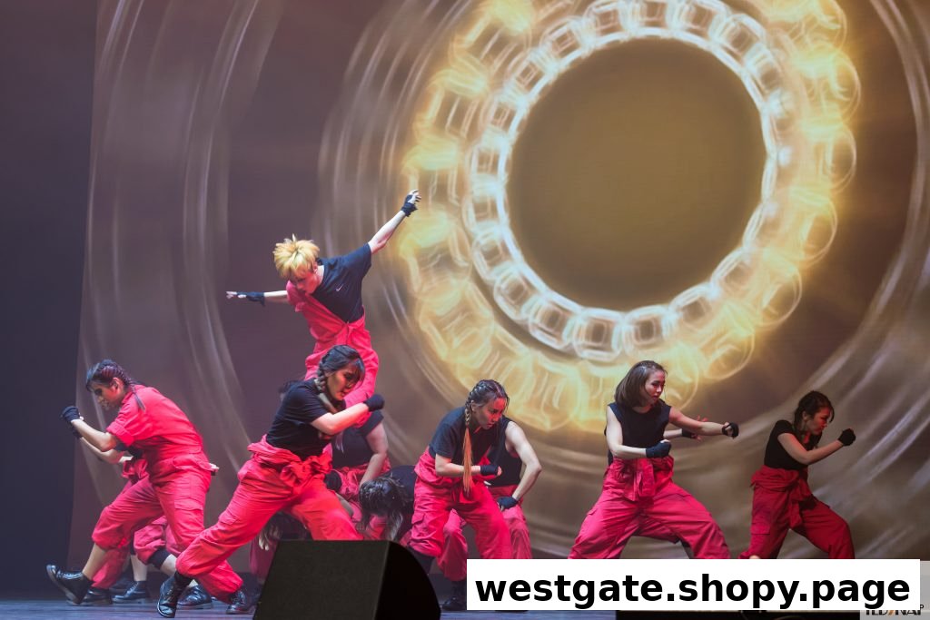 A group of dancers in red and black performing on a stage with a dynamic light projection.