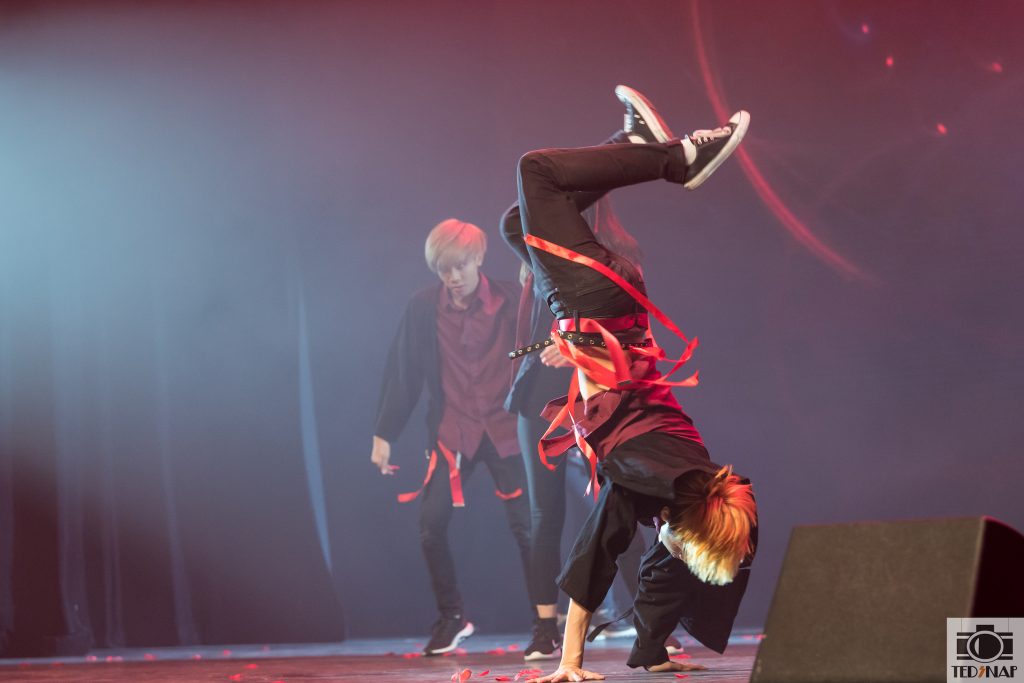 Performers showcase dynamic moves on stage with red ribbons and dramatic lighting.