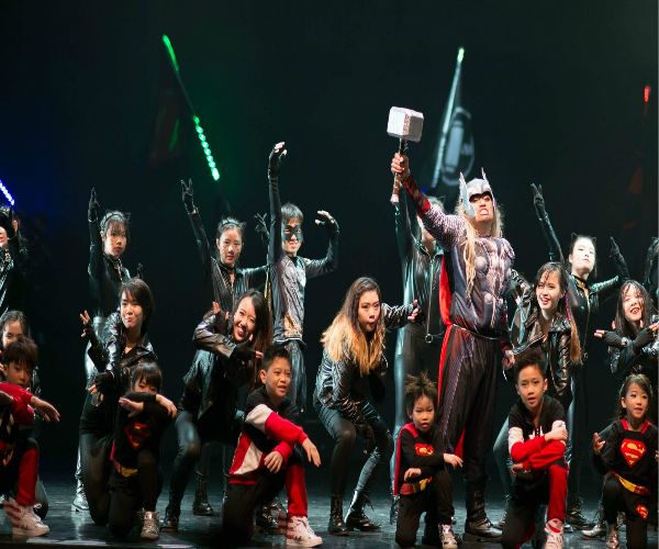 Students of DF Academy perform in superhero costumes on stage.