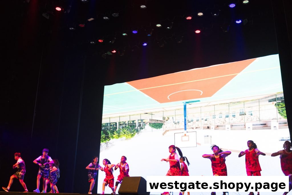 Children in sports attire perform on a stage with a basketball court projection behind them.