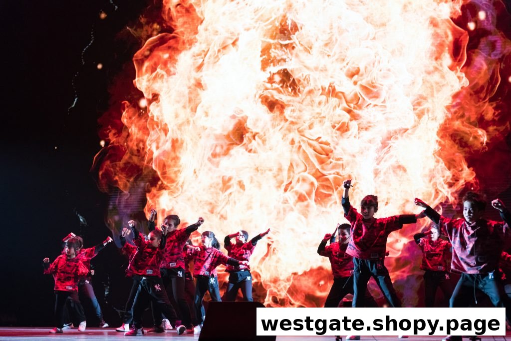 Children in red and black outfits perform on stage with a dynamic fiery background display.