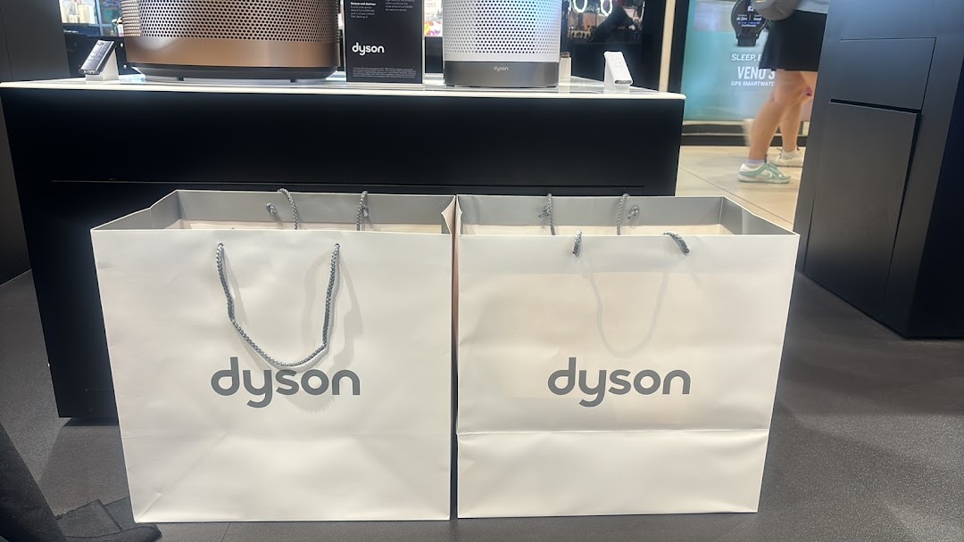 Two Dyson shopping bags sit before display models of Dyson air purifiers in a retail store.