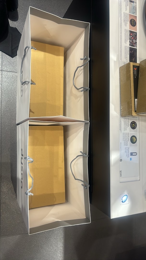 Two Dyson shopping bags filled with products, placed next to a bright product display inside the store.