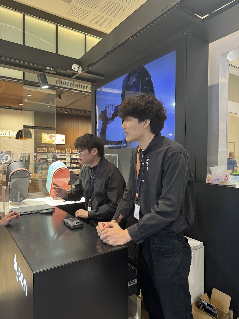 Dyson staff assist customers at a counter, showcasing innovative products and technology.