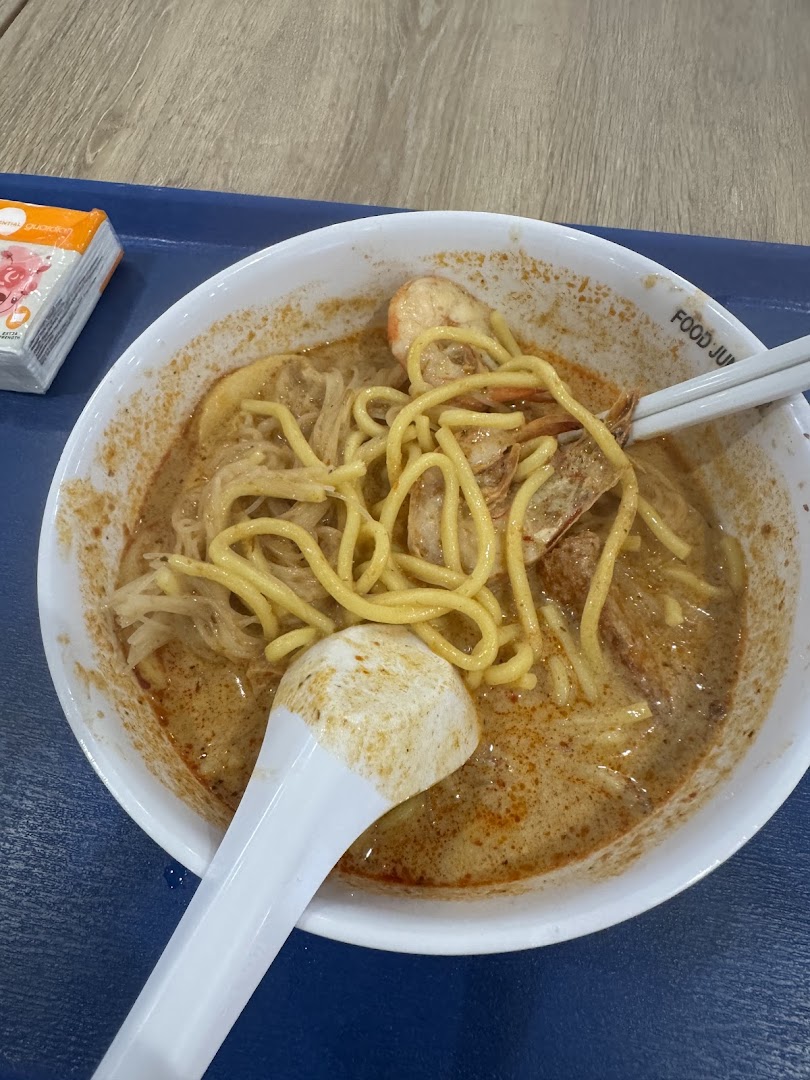A close-up of a delicious bowl of laksa noodles with prawns and a rich, spicy broth.