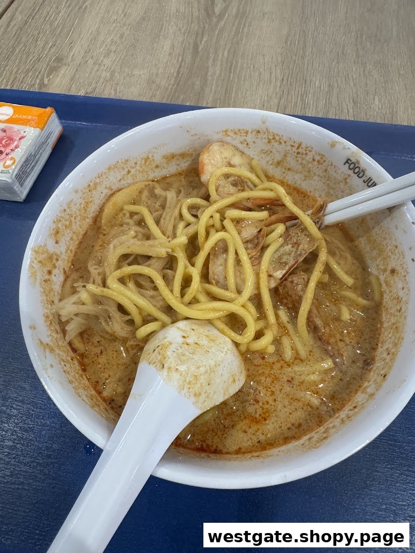 A close-up of a delicious bowl of laksa noodles with prawns and a rich, spicy broth.