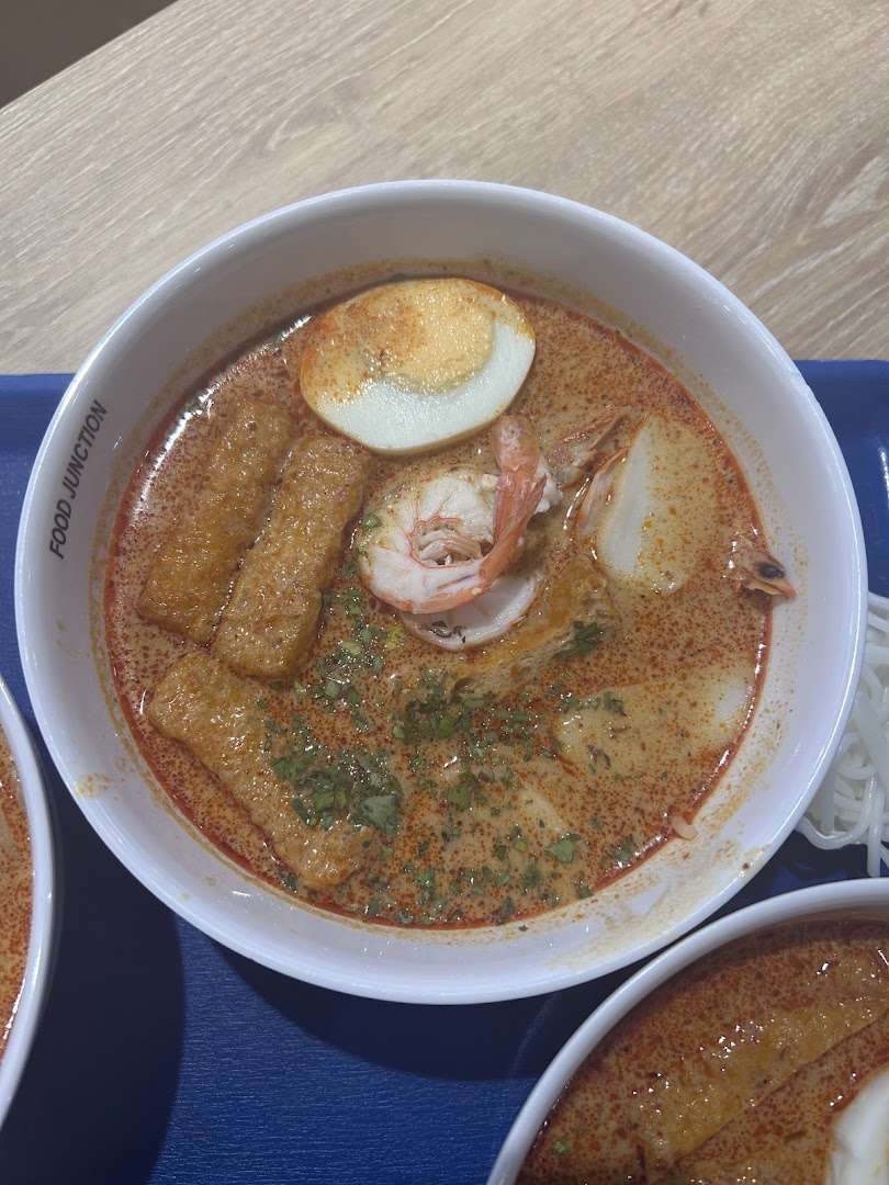 A vibrant bowl of spicy laksa with prawns, egg, and fishcake, served at Food Junction.