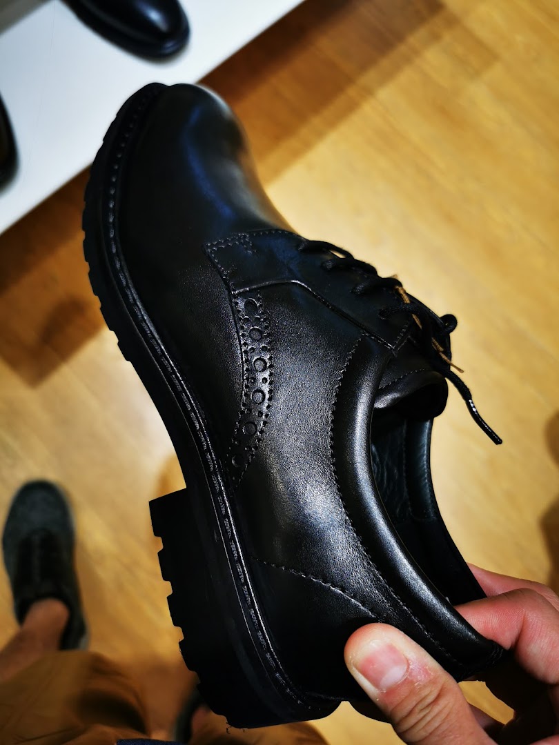 A hand holds a black leather ECCO shoe, showcasing its design and textured sole.