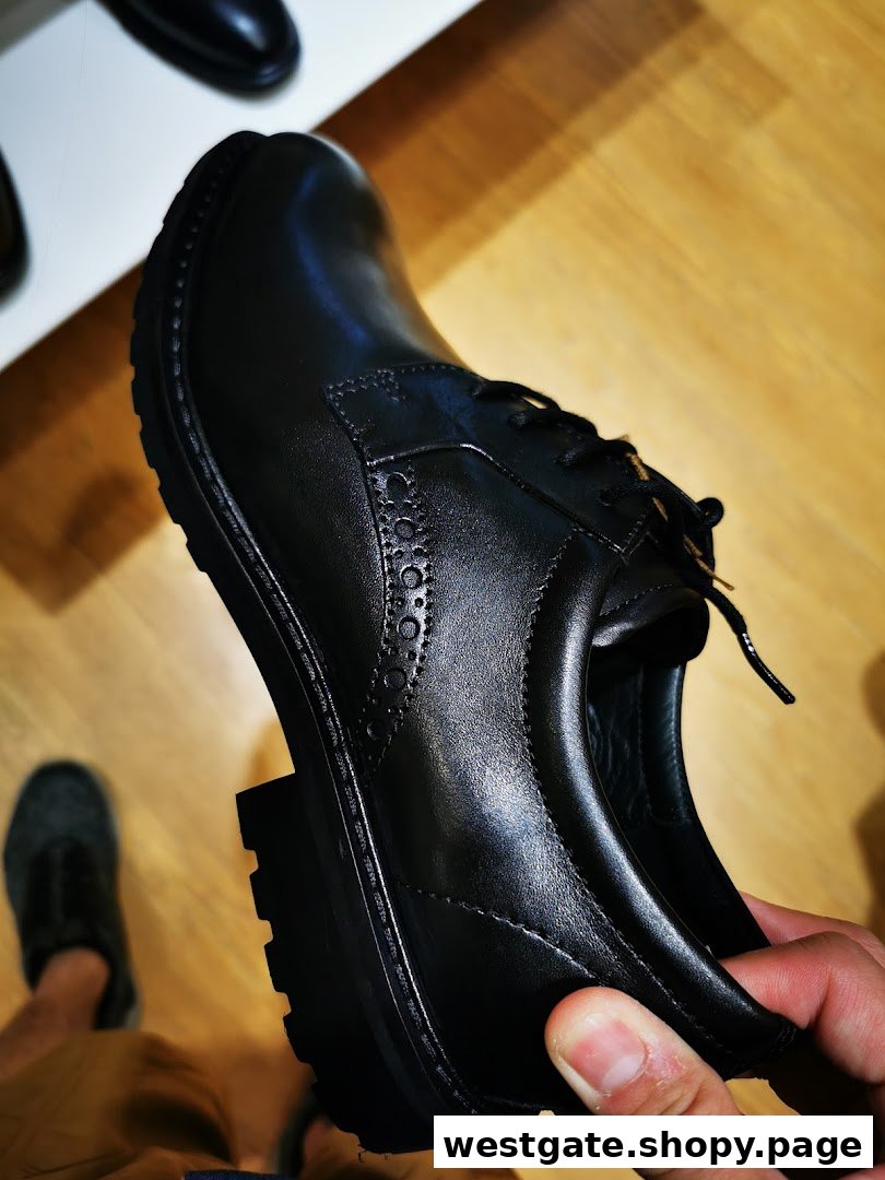 A hand holds a black leather ECCO shoe, showcasing its design and textured sole.