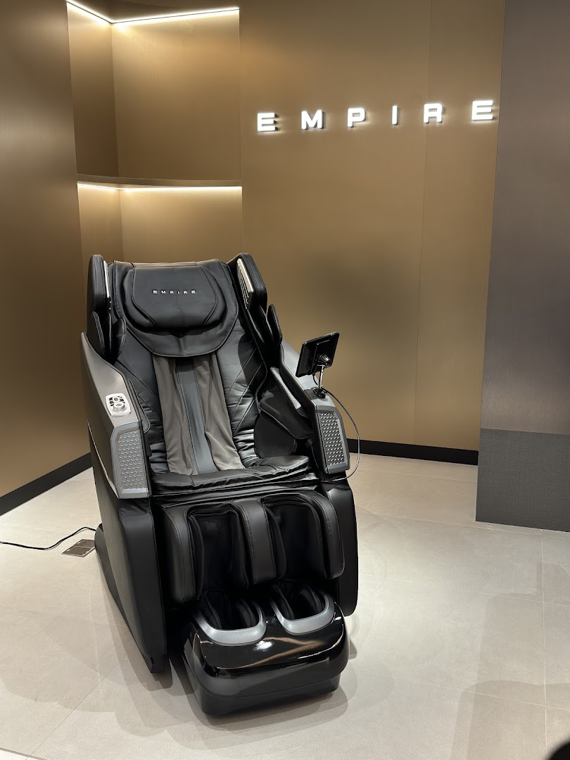 A luxurious black massage chair displayed in a modern showroom with the EMPIRE logo.