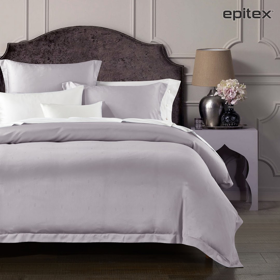 An elegantly styled bed featuring luxurious grey and white bedding from Epitex, complete with decorative pillows.