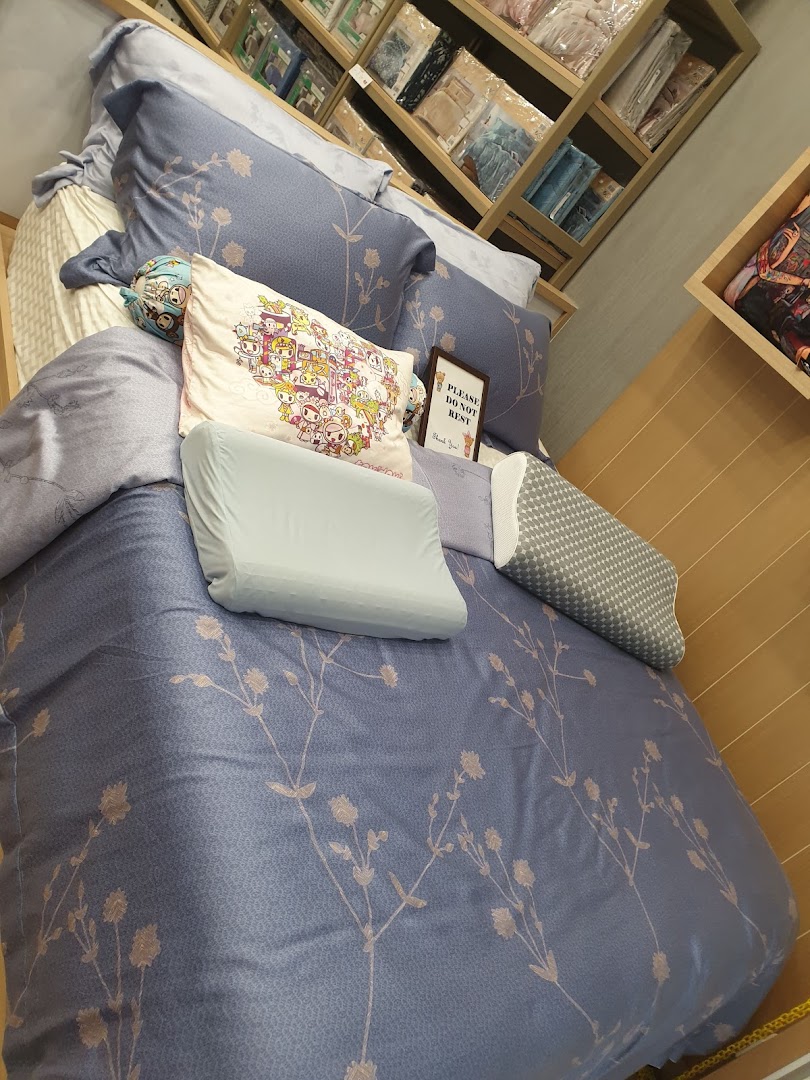 A display bed with blue floral bedding, various pillows, and shelves of textiles in Epitex.