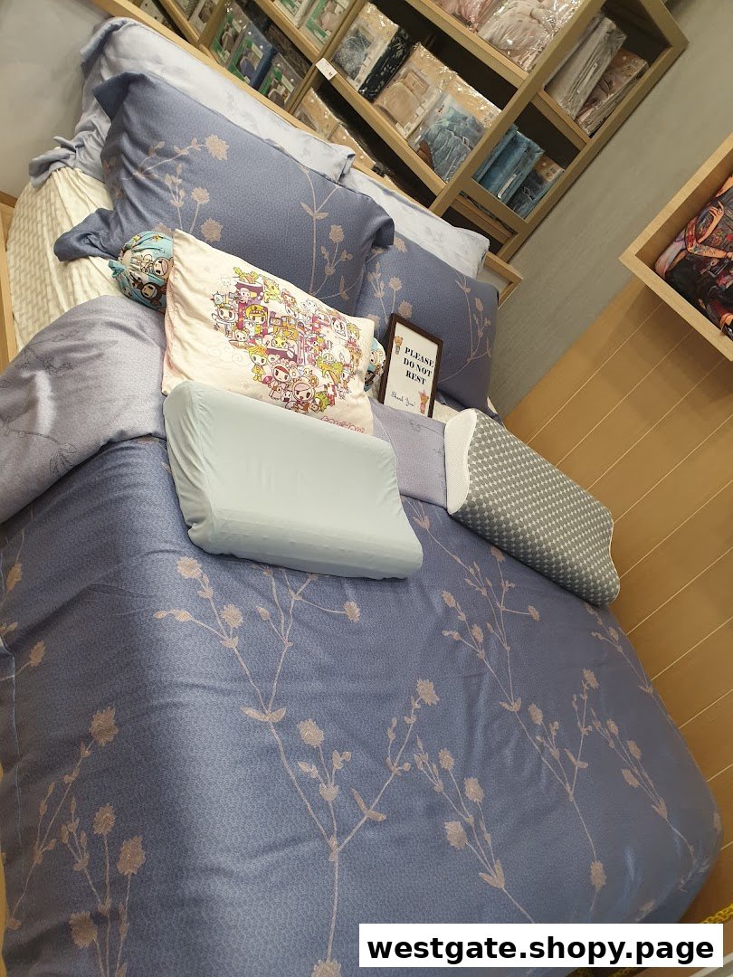 A display bed with blue floral bedding, various pillows, and shelves of textiles in Epitex.