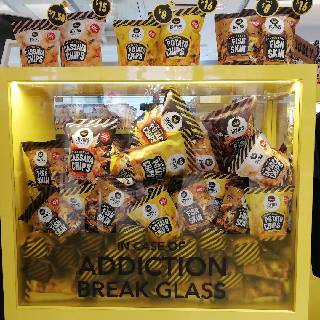 A vibrant yellow display case showcasing various Irvins Salted Egg snacks, including chips and fish skin.