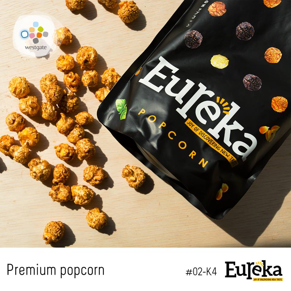 A bag of Eureka Popcorn with scattered popcorn kernels on a light wooden surface.