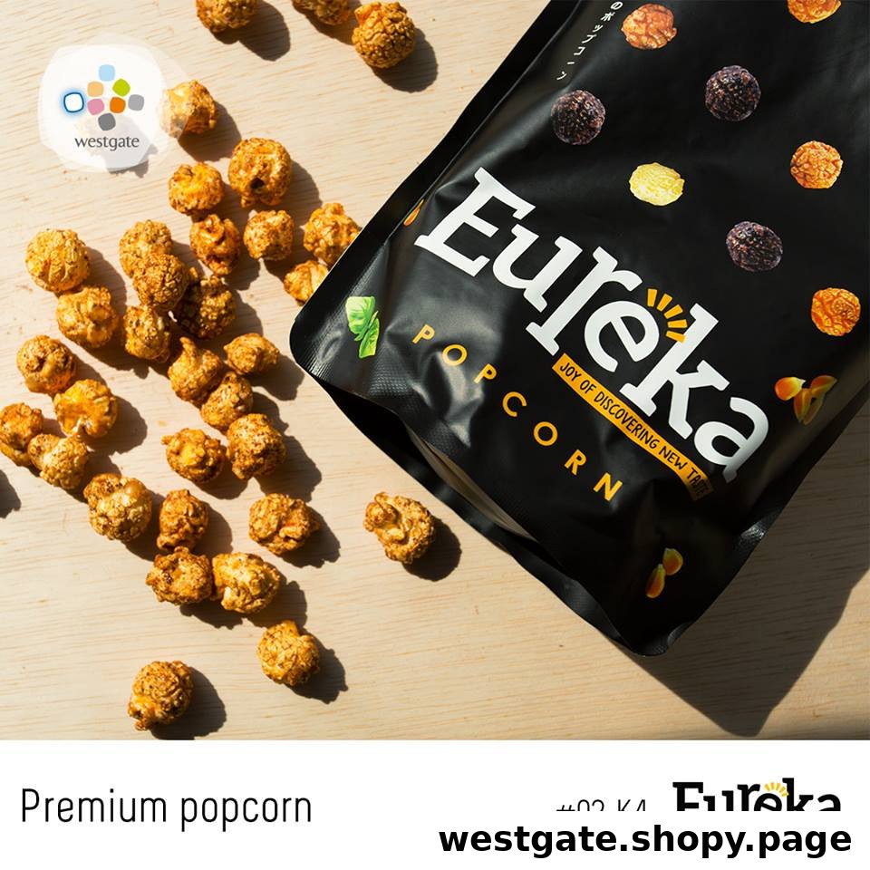A bag of Eureka Popcorn with scattered popcorn kernels on a light wooden surface.