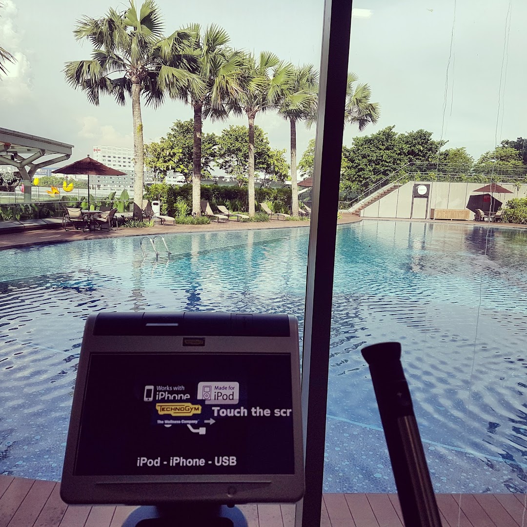 A gym equipment screen overlooks a large outdoor swimming pool surrounded by palm trees and lounge areas.