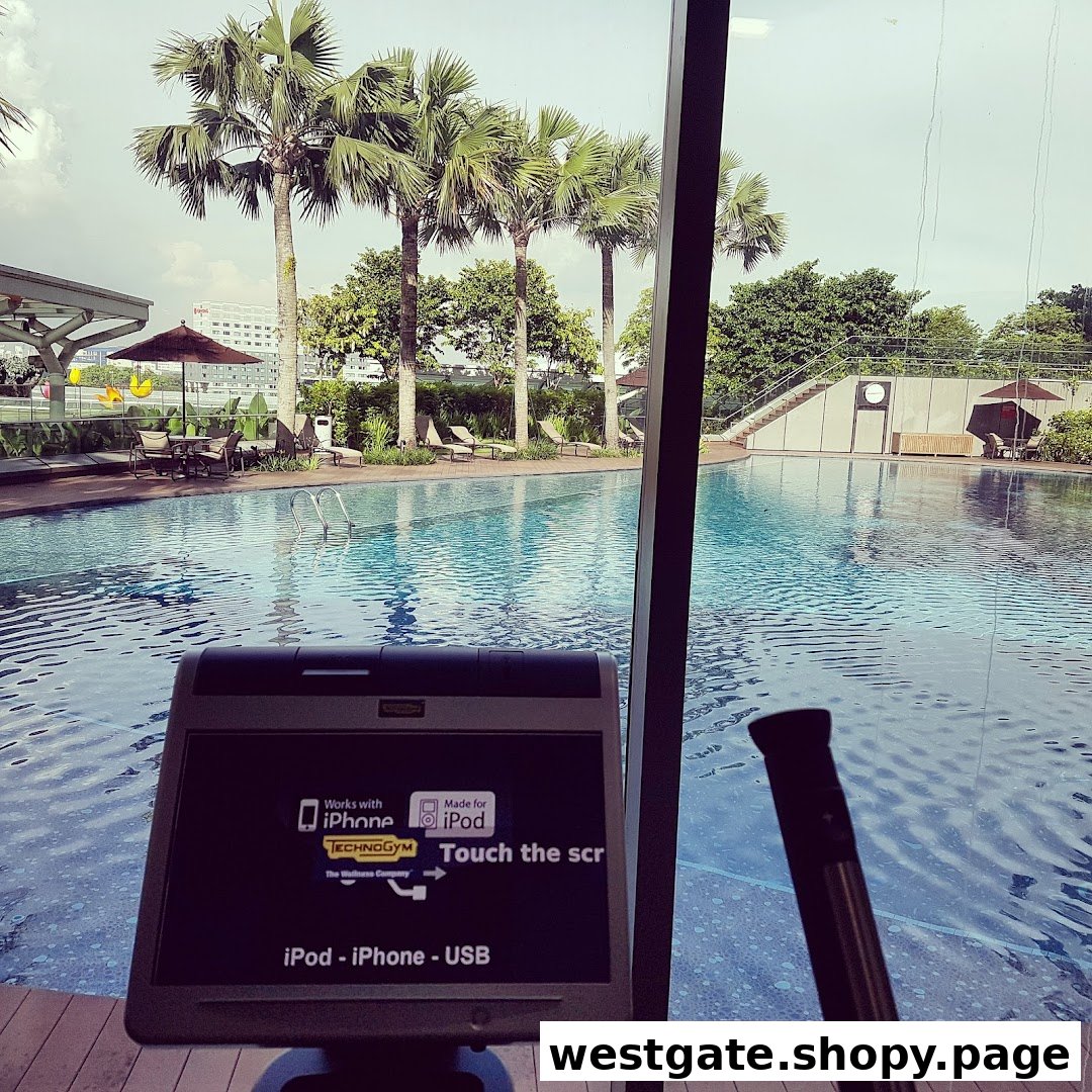 A gym equipment screen overlooks a large outdoor swimming pool surrounded by palm trees and lounge areas.