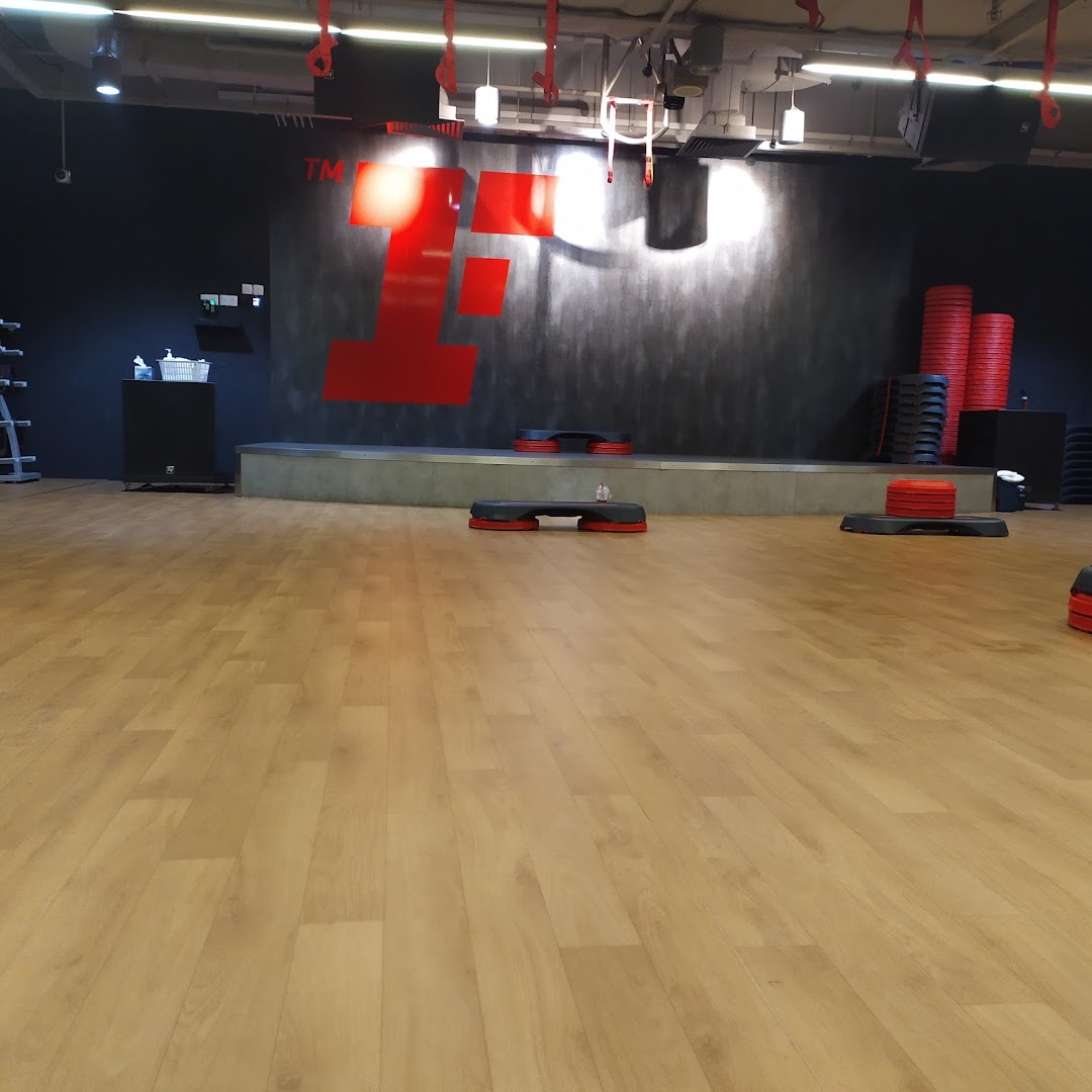 An empty fitness studio with a large red 'F' logo, a stage, and various exercise equipment.